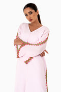 Dubai woman wearing a light pink dress with floral embroidery on a white studio background